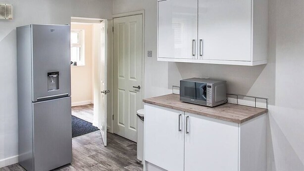 Una cocina con refrigerador, microondas y gabinetes blancos.