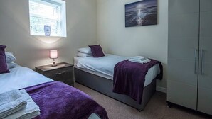 Un dormitorio con dos camas, una ventana con persianas, una lámpara de noche, un armario y un cuadro en la pared.