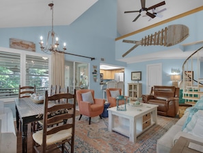 A spacious living room with a large window, a chandelier, a ceiling fan, and a wooden fish decoration. - Bright and Cheerful Cottage, Updated Kitchen, Large Flat Screen TV (Miramar Beach)