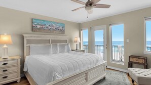 A bedroom with a bed, two bedside tables with lamps, a ceiling fan, a painting, and a view of the ocean through a door. - Directly on the Gulf, Free Beach Chairs, Comfy Escape (Miramar Beach)