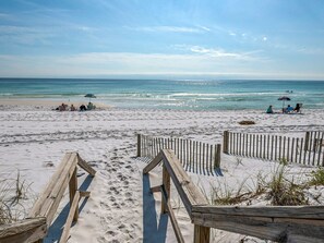 Une plage de sable avec des allées en bois et des gens qui se détendent sous des parasols.