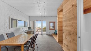 A modern interior with a wooden dining table, chairs, and a view of the beach through an open door. - Directly on the Gulf, Free Beach Chairs, Comfy Escape (Miramar Beach)