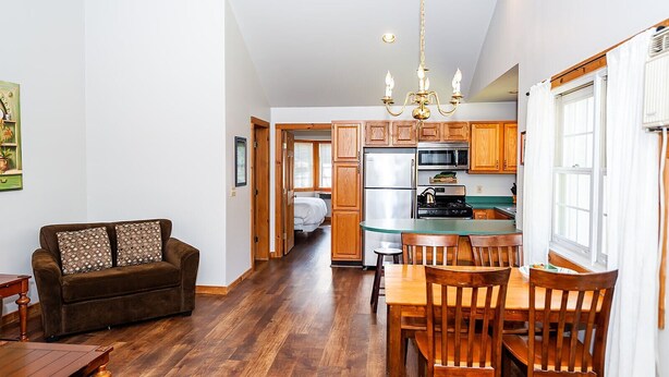 A modern kitchen with wooden cabinets, a stainless steel refrigerator, and a dining area with wooden chairs and a table.