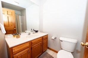 Un bagno con un mobile lavabo in legno, un lavandino bianco, uno specchio, un water e una tenda per la doccia.