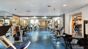 Un gimnasio con diferentes máquinas de ejercicio, suelo azul y espejos en las paredes.