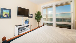 Une chambre à coucher avec un lit, une télévision, une plante et une fenêtre donnant sur un beau paysage.