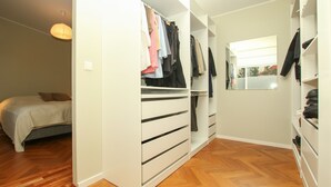 Ein Schlafzimmer mit Bett, begehbarem Kleiderschrank mit Kleidung und einem Spiegel.
