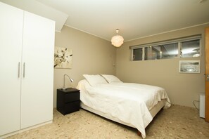 A bedroom with a bed, a nightstand, a wardrobe, a window, and a light fixture.