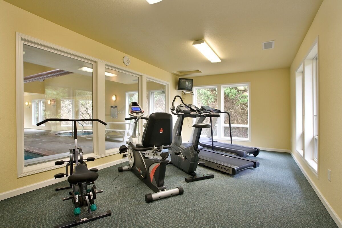 A gym with cardio machines, weight equipment, and large windows.