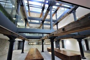 Un vaste atrium doté de hauts plafonds, de poutres apparentes et d’une grande table en bois placée au centre.