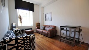 A living room with a brown leather sofa, a patterned ottoman, a black and white sofa, and a metal bar stool. - Royal William Yard Apartment (Plymouth)