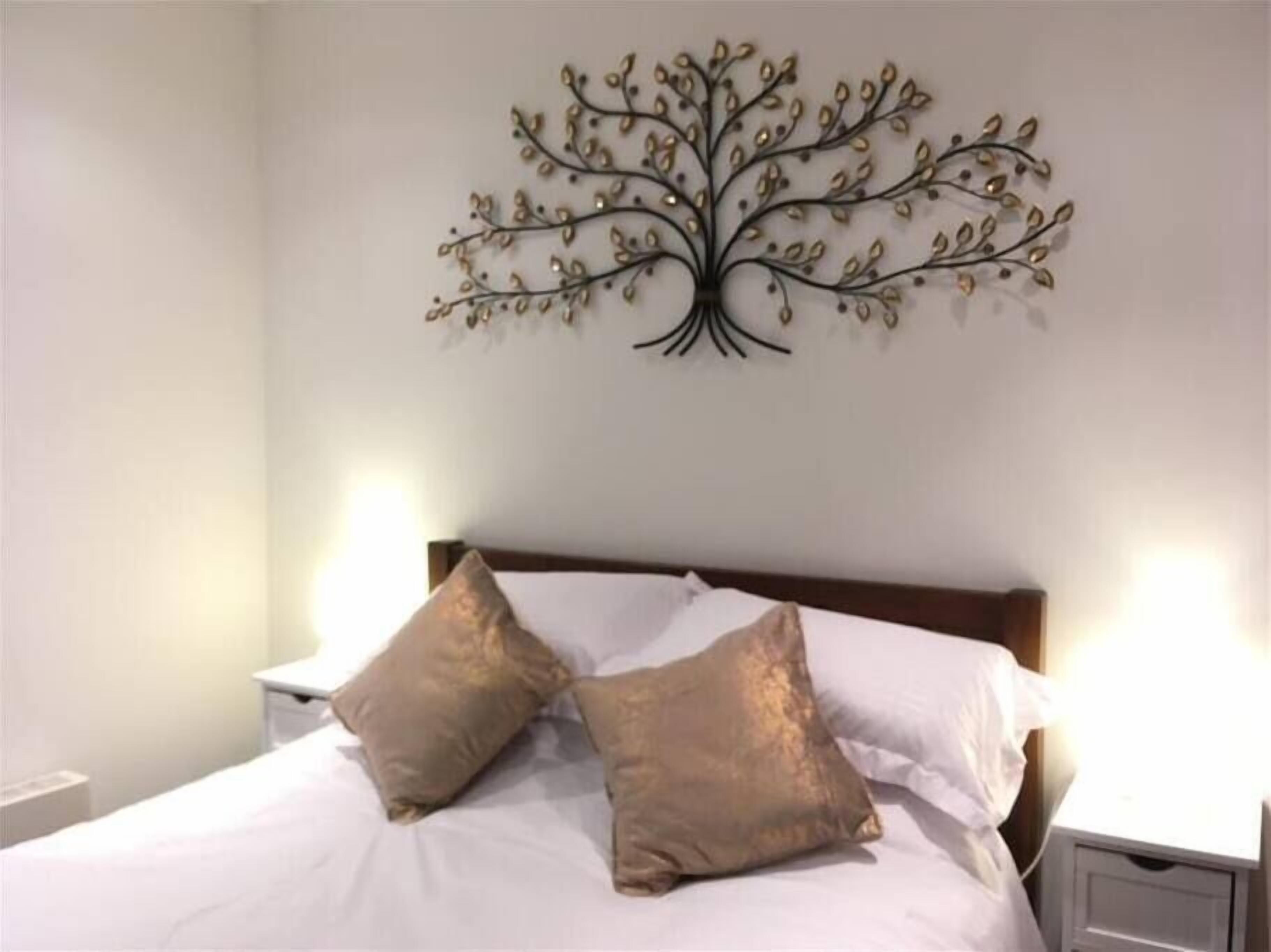 A bedroom with a bed, two pillows, a nightstand, and a wall-mounted tree decoration.