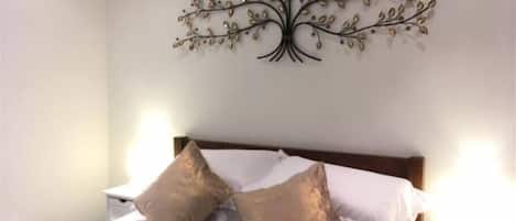 A bedroom with a bed, two pillows, a nightstand, and a wall-mounted tree decoration.