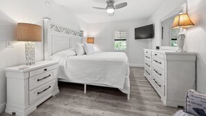 A bedroom with a bed, a nightstand, a dresser, a ceiling fan, a TV, and a window with blinds. - Newly Renovated Waterfront Dock View 2 bed, 2 bath at Sanibel Moorings #1431 (Sanibel)
