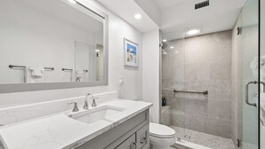 A modern bathroom with a large mirror, two sinks, a toilet, and a glass-enclosed shower. - Newly Renovated Waterfront Dock View 2 bed, 2 bath at Sanibel Moorings #1431 (Sanibel)
