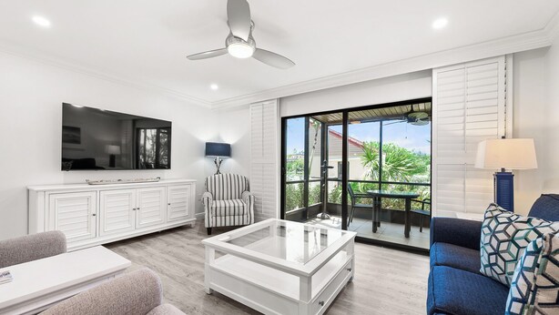 A modern living room with a flat-screen TV, a ceiling fan, a glass coffee table, a striped armchair, and a sofa with patterned cushions. - Newly Renovated Waterfront Dock View 2 bed, 2 bath at Sanibel Moorings #1431 (Sanibel)
