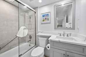 A modern bathroom with a glass-enclosed shower, a white toilet, a vanity with a mirror, and a framed beach painting. - Newly Renovated Waterfront Dock View 2 bed, 2 bath at Sanibel Moorings #1431 (Sanibel)