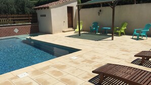 Una piscina con piso de baldosas, una pérgola de madera y varias sillas coloridas.