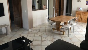 Un comedor amplio con una mesa y sillas de madera, una cocina al fondo y un televisor montado en la pared.