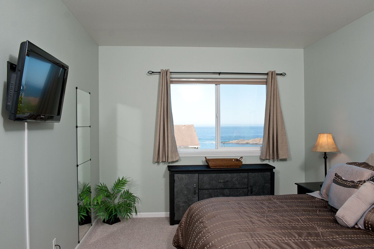 Een slaapkamer met een bed, een televisie aan de muur, een raam met gordijnen, een dressoir en een lamp.