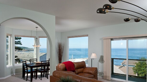 A spacious living room with a view of the sea, a dining area, and a large window.