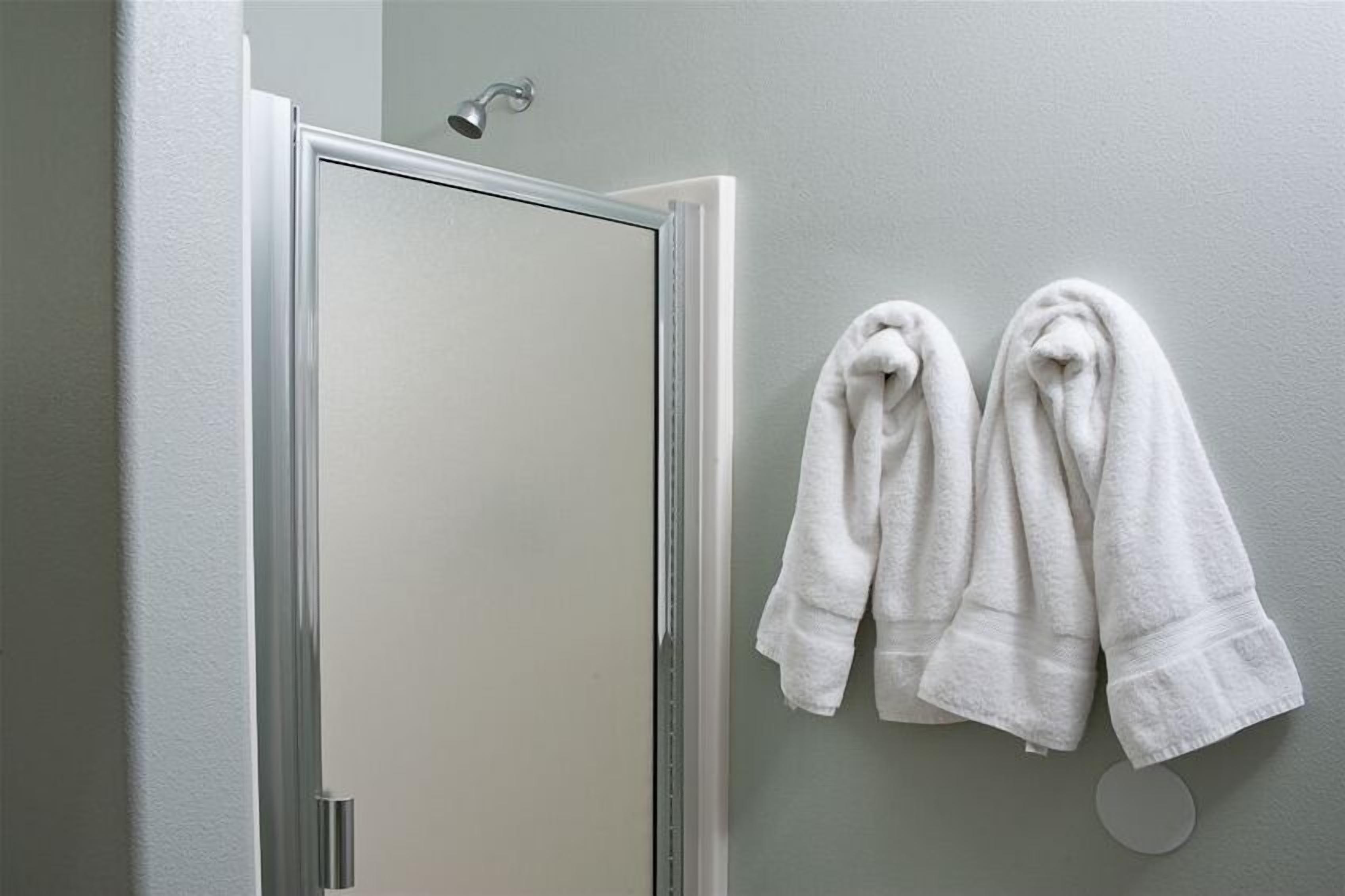 Un baño con ducha, dos toallas colgadas en una pared y un espejo redondo.
