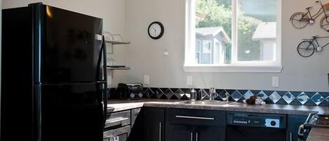 A kitchen with a black refrigerator, a dishwasher, and a window with a view of houses and bicycles outside.