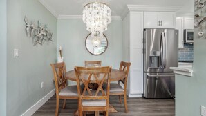 A dining area with a round wooden table and chairs, a chandelier, and a stainless steel refrigerator.