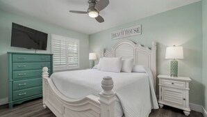 A bedroom with a white bed, teal dresser, and a ceiling fan.