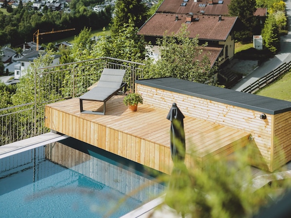 A rooftop pool area with a lounge chair, a small potted plant, and a wooden deck.