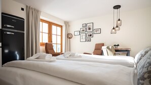 A hotel room with two beds, a desk, a chair, a wardrobe, and a window with curtains. - Landhaus Lodges Kaprun - Franz, infinity pool & garden (Kaprun)