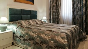 Ein Schlafzimmer mit einem großen Bett, zwei Nachttischen, einem Kopfteil, einem Gemälde an der Wand und gemusterten Vorhängen.