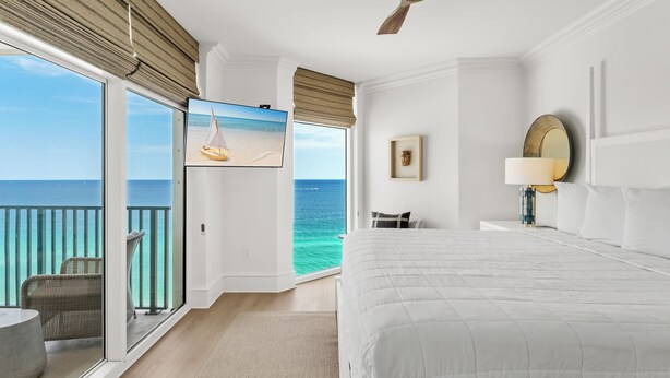 A hotel room with a large bed, a TV mounted on the wall, a balcony with a view of the ocean, and a ceiling fan. - Gulf Front, Corner Condo, Sunrise Views, Pool (Destin)