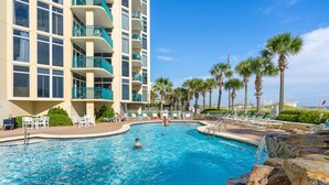 A swimming pool with lounge chairs and palm trees, surrounded by a multi-story building with balconies. - Gulf Front, Corner Condo, Sunrise Views, Pool (Destin)
