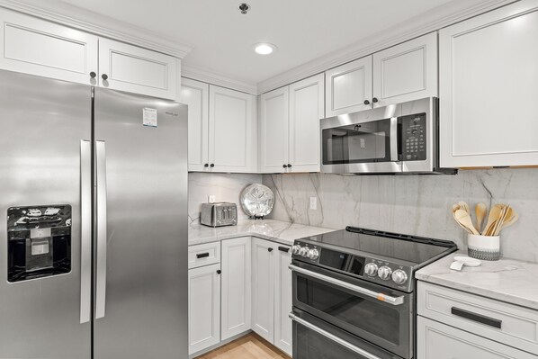 A modern kitchen with stainless steel appliances, white cabinetry, and a marble countertop.