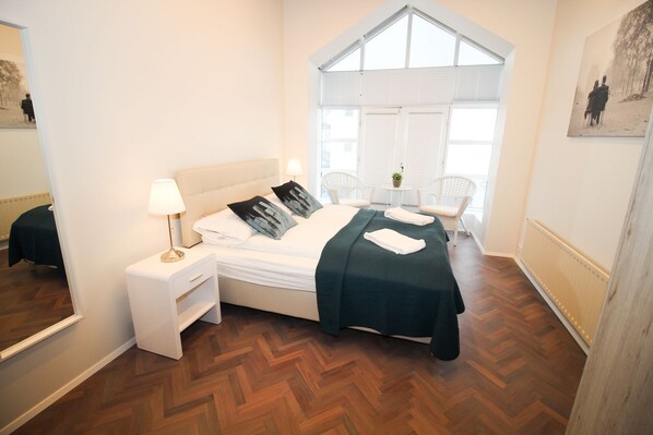Quarto com cama, mesa de cabeceira e janela com persianas.