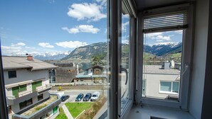 Une vue depuis une fenêtre donnant sur un parking rempli de voitures, un bâtiment doté d’un toit végétalisé et, au loin, des montagnes enneigées.