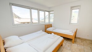 Une chambre avec deux lits en bois, du linge de lit blanc et de grandes fenêtres donnant sur une vue sur les montagnes.