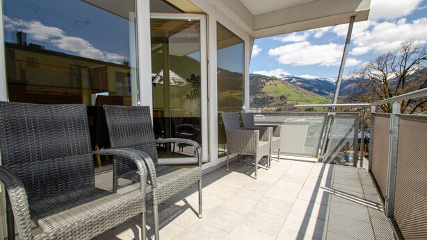 Un balcon extérieur avec des meubles en osier, une porte vitrée donnant sur une pièce et une vue sur les montagnes.