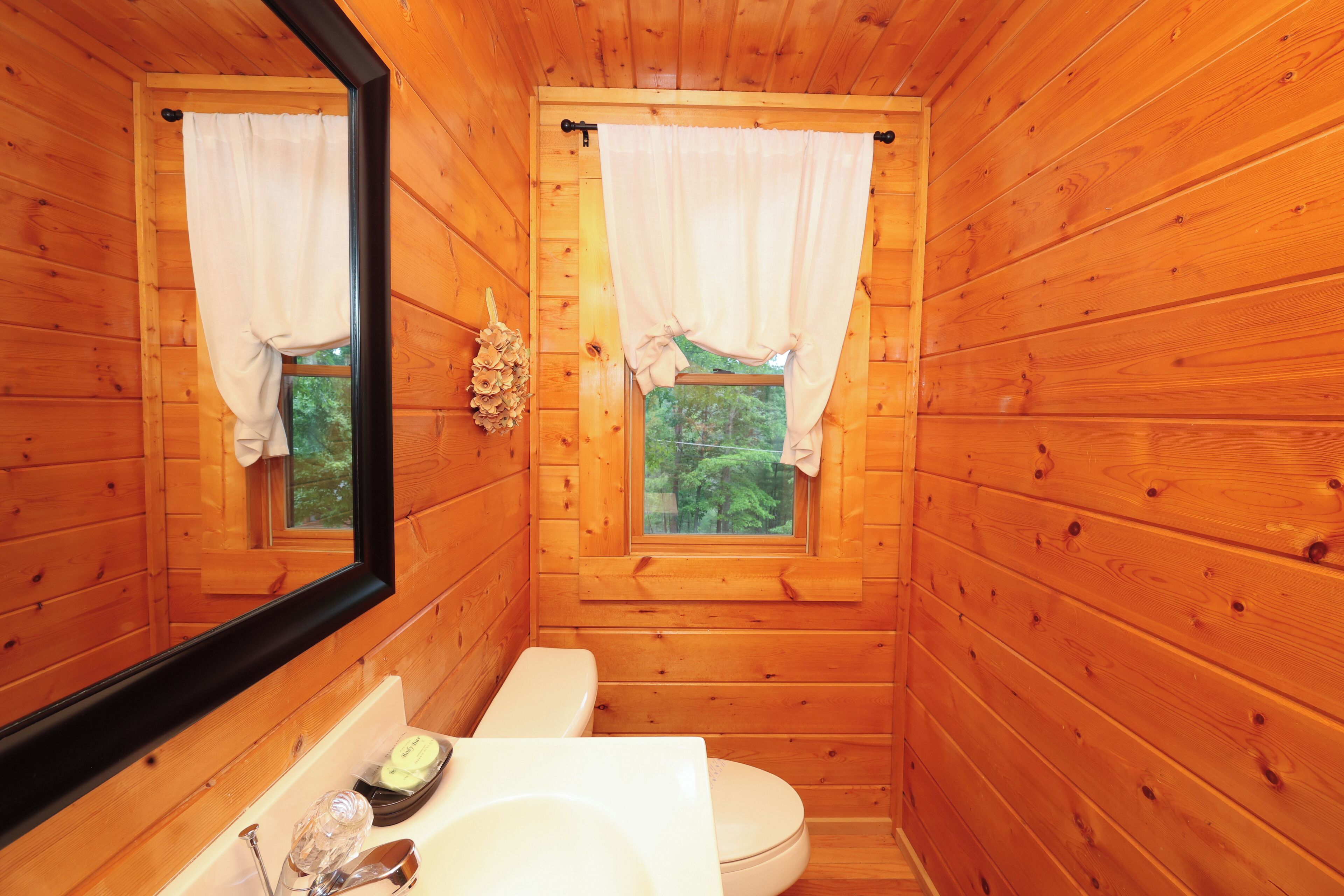 Baño de cabaña de madera con inodoro, lavamanos y espejo.