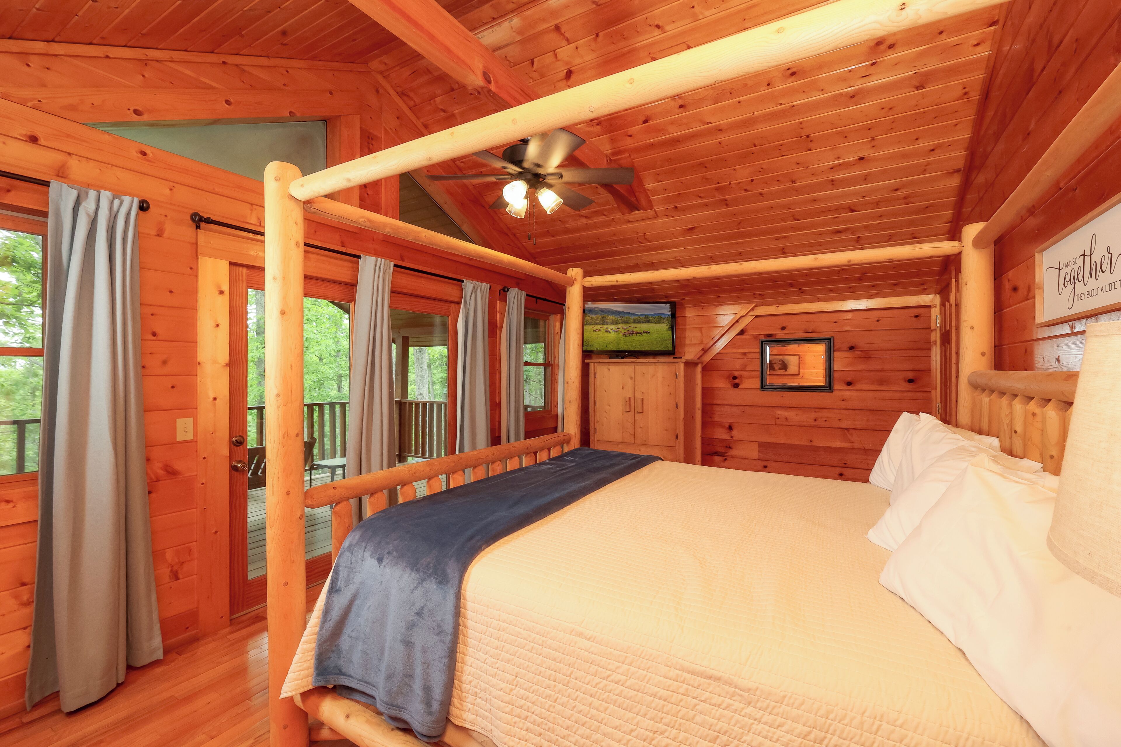 A wooden cabin bedroom with a bed, a ceiling fan, and a TV on the wall.