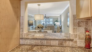 A kitchen with granite countertops, a dining area with wicker furniture, and a view into the living room. - Best location on Siesta Key/Crescent Beach - just steps to the water! (Sarasota)