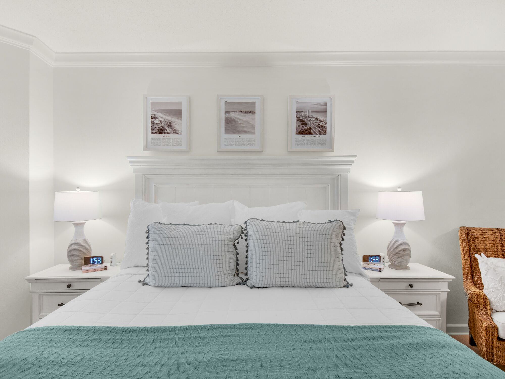 A neatly arranged bedroom with a bed, two bedside tables with lamps, a clock, and three framed pictures on the wall.