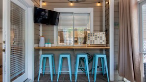 Una cucina compatta con un piano di lavoro in legno, una TV montata sopra e tre sgabelli blu.