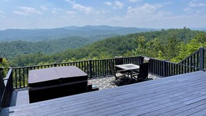 A deck with a table and chairs, overlooking a forested mountain range. - Mountain Cabin,Panoramic View,Hot Tub, WiFi, Fire Table (Ferguson)