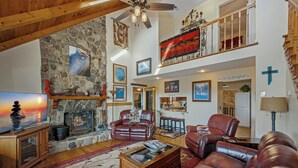 A spacious living room with a stone fireplace, leather sofas, and a high ceiling with a balcony. - Mountain Cabin,Panoramic View,Hot Tub, WiFi, Fire Table (Ferguson)