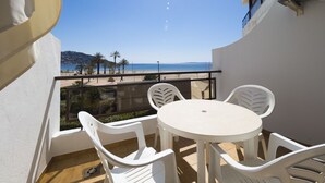 Ein Balkon mit weißem Tisch und Stühlen, der Blick auf einen Strand mit Palmen und einen klaren Himmel bietet.