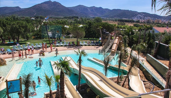 A water park with multiple slides and a swimming pool, surrounded by palm trees and mountains in the background. - Nice apartment in front of the sea in Roses Inmosantos Oasis B5 (Rosas / Roses)