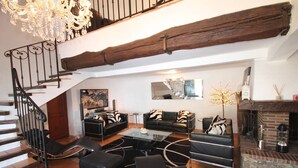 A spacious living room with a staircase, black leather sofas, a glass coffee table, and a fireplace. - Large sea-view villa with 3 independent apartments (Mandelieu-la-Napoule)