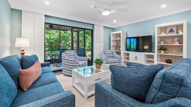 A living room with blue sofas, a glass coffee table, a TV, and a bookshelf.